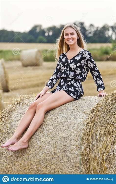 attractive blonde sitting on straw ball in summer dress smiling and