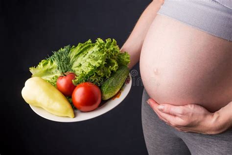 pregnant woman belly holding a plate with vegetables concept for