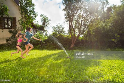 girl and her little sister having fun with lawn sprinkler in the garden