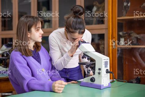 high school girl letting her classmate look through microscope