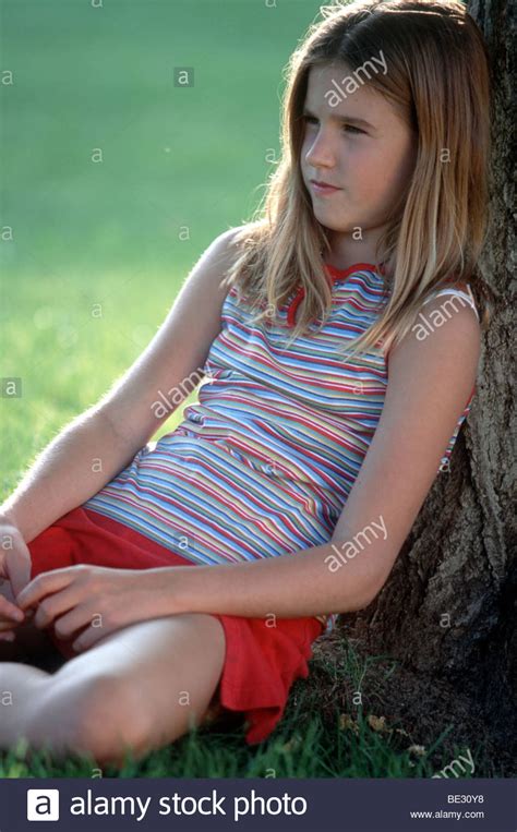 preteen girl sit against tree in park pensive mood stock