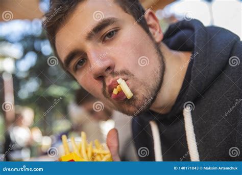 Young Man Is Greedily Eating His Burger While Sitting At The