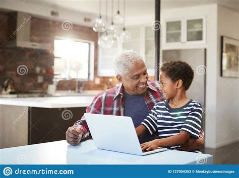 grandfather and grandson sitting around table at home using laptop