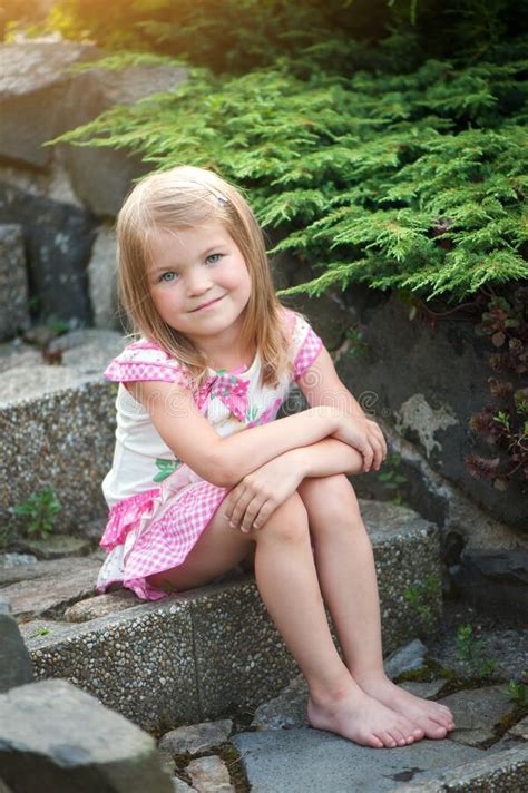 Девочка в платье сидит на каменных шагах в сад Босые ноги улыбаются