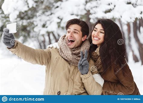 couple taking selfie on phone standing in winter forest panorama stock
