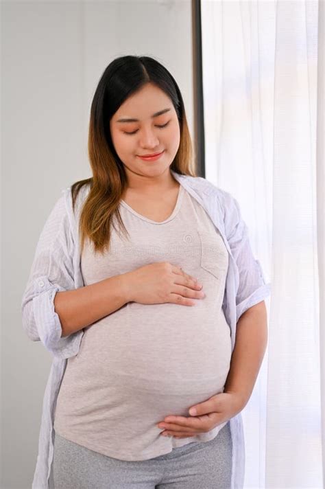 Relaxed And Happy Asian Pregnant Woman In Casual Clothes Feeling Her