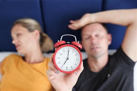 Sleepy Man And Woman Lying In Bed And Holding Red Alarm Clock Closeup