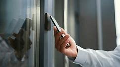 Close up of male hand unlocking door using mobile phone application. Unlocks a modern office building. Scanning open smartphone with mock up screen app. Smart electronic locks with keyless access
