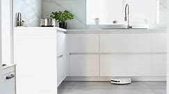 The automated robot vacuum cleaner is cleaning the floor in the kitchen. Automatic electric cleaning inside the apartment. Robotic cleaner technology. Modern technologies in-house. Home cleaning