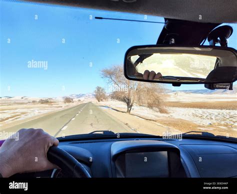 A hand grips the steering wheel while driving on a road in winter ...