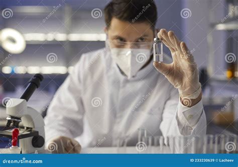 Focused Serious Doctor Scientist in a Medical Laboratory Looks at a Glass Ampoule with New Drugs ...
