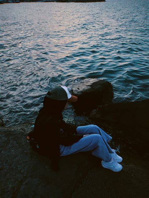 Woman in Cap Sitting on Rocks on Lakeshore · Free Stock Photo