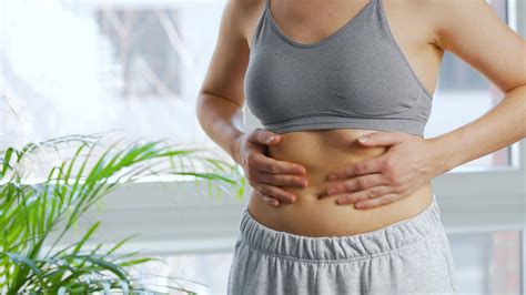 Woman compressing the skin on her stomach checking for cellulite and excess subcutaneous fat ...