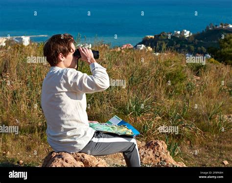 Adventurous young Spanish male traveler sitting on a rock using ...