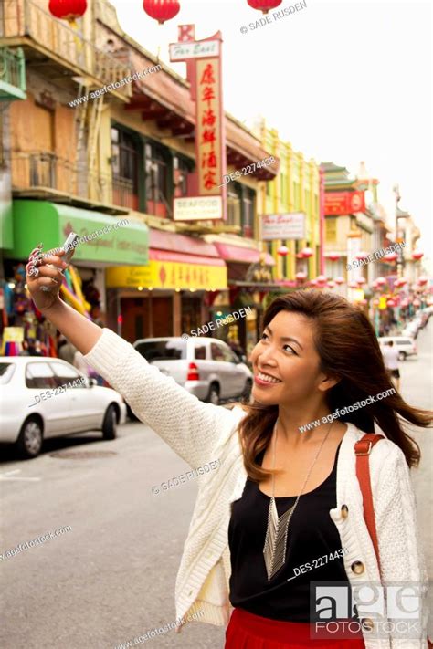 A woman takes a picture of herself with her cell phone camera in a busy ...