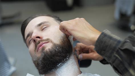 Barber uses straight razor to shave man's neck and face to shape facial ...