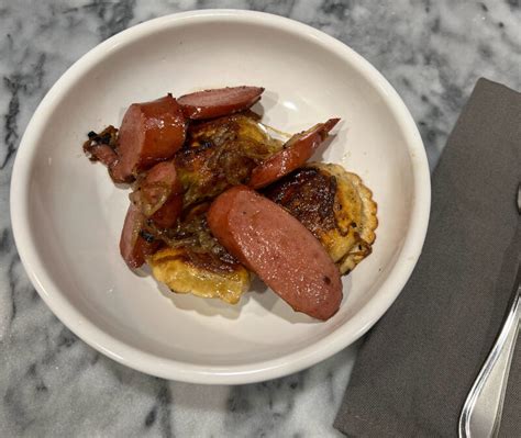 A plate with pierogies sausages and cabbage served with a small bowl of sour cream