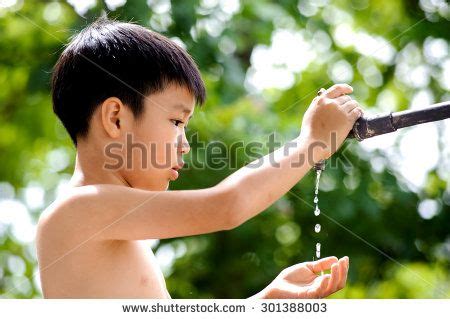 Close up kid hand open for water drop from old grunge brass faucet on green bokeh from tree ...
