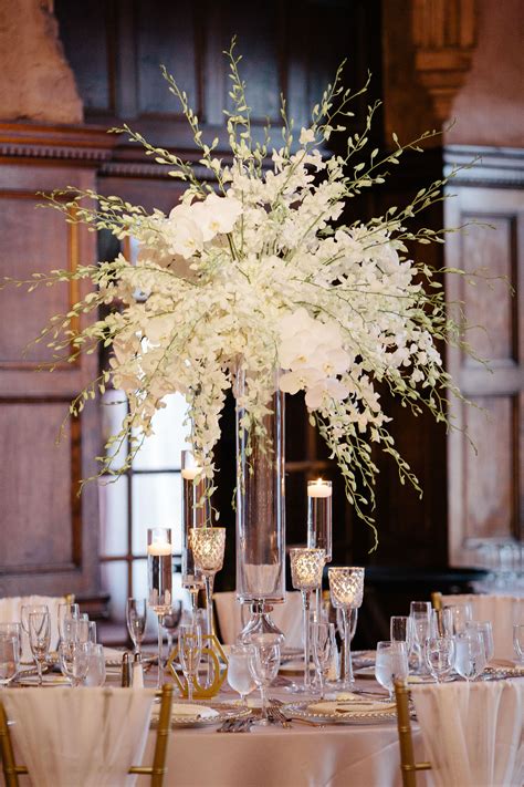 a tall vase filled with white flowers sitting on top of a table covered ...