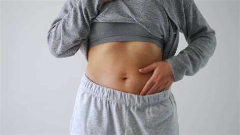 Woman compressing the skin on her stomach checking for cellulite and excess subcutaneous fat ...