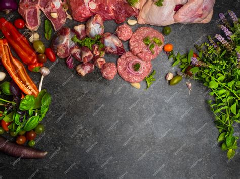 Surtido de carne cruda sobre fondo oscuro con tomates cherry, hojas de ...