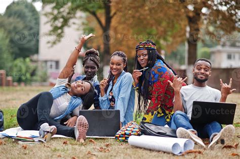 Group of five african college students spending time together on campus at university yard ...