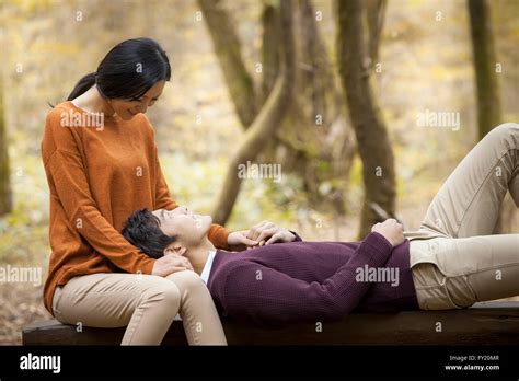 Woman seated on a bench and a man lying on her lap looking at her at ...