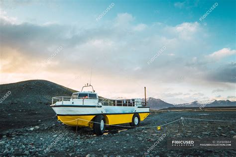 White and yellow boat with wheels standing at stony hill, Skaftafell ...