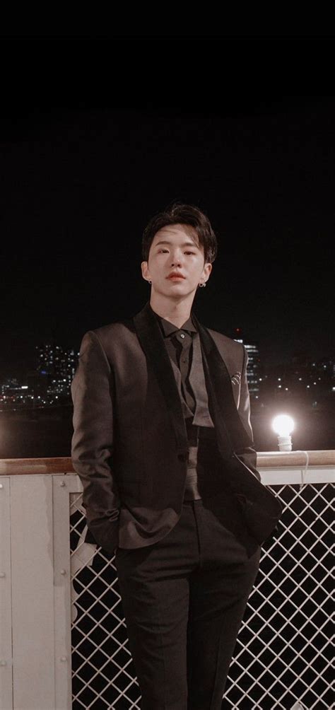 a young man in a suit and tie standing on a rooftop at night with city ...