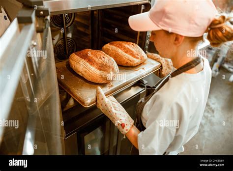 Woman in pink cap takes breads out of oven in craft bakery workshop ...