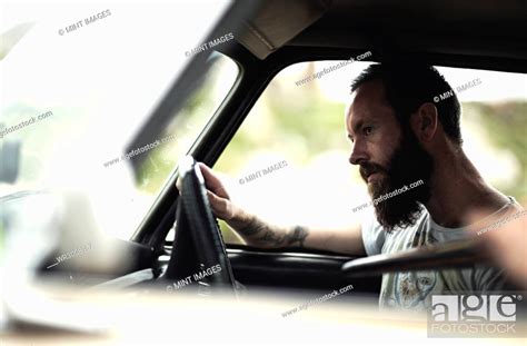 Side view of bearded man sitting behind the steering wheel of a car ...