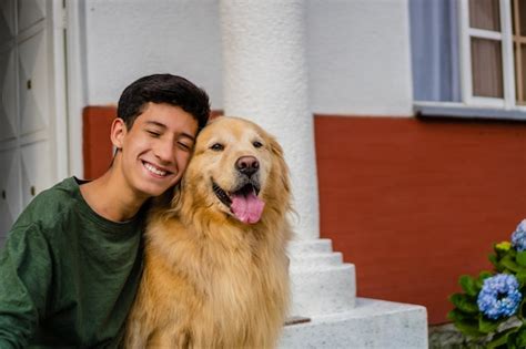 Latin teenager hugging his golden retriever dog sitting in the driveway ...