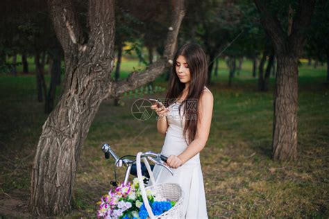 身穿白裙子的女孩和手拿着智能手机的背心站在一辆自行车旁边高清图片下载-正版图片506509637-摄图网