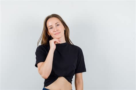 Young female propping chin on hand in black blouse and looking cheery ...