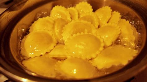 Ravioli cooks in wobbly pan of boiling water in warm light close up ...