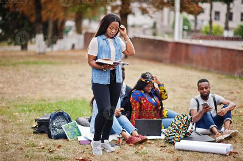 Group of five african college students spending time together on campus at university yard ...