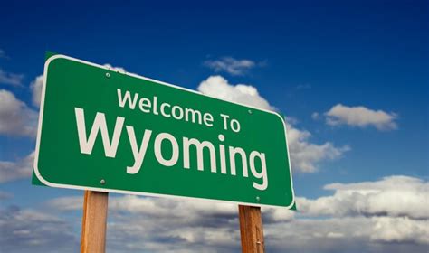Welcome to wyoming green road sign over blue sky with some clouds ...