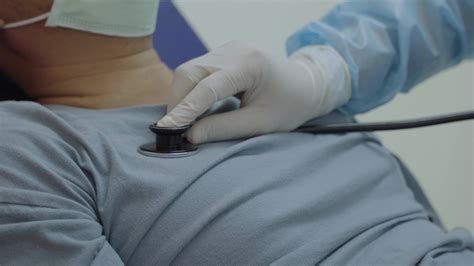 close up on hands of doctor placing stethoscope on chest of male patient to hear heart rate and ...