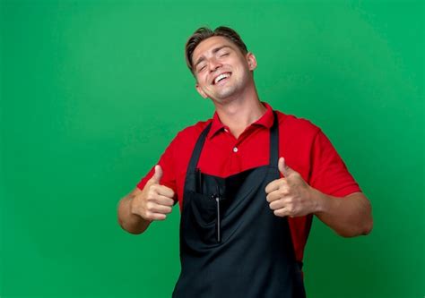 Jeune coiffeur blond heureux en uniforme Thumbs up isolé sur un espace ...