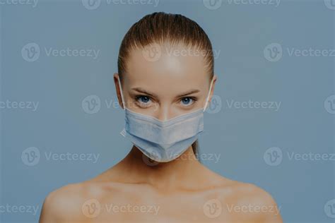 Studio shot of naked European woman wears disposable medical mask as prevention fromm ...