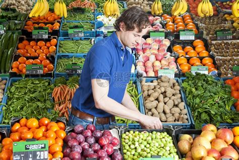 创建在一家商店里各种新鲜水果和蔬菜箱中工作的一个绿色杂货店员男人柜台高清图片下载-正版图片307849083-摄图网