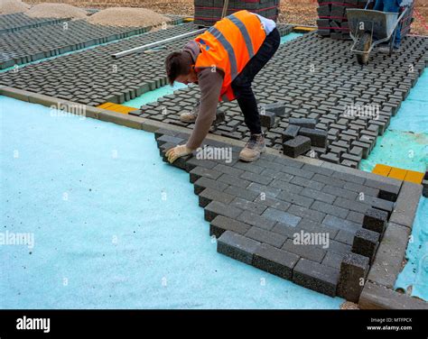 Construction worker laying interlocking paving concrete onto sheet ...