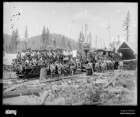 This Lee Moorhouse photograph shows a logging crew on a flatcar and standing around a locomotive ...