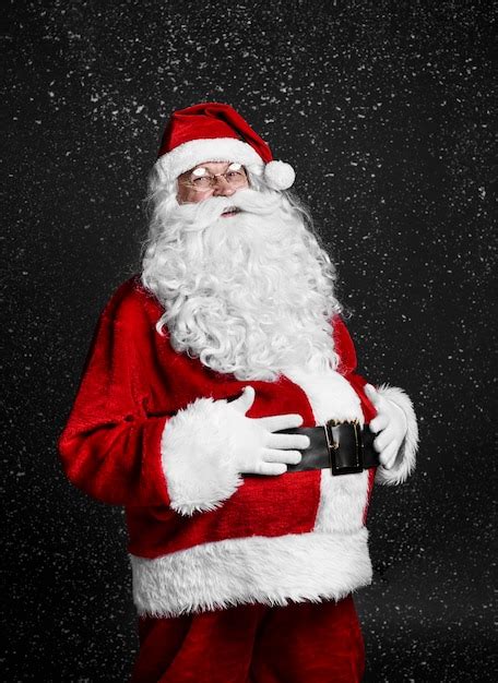 Cheerful santa claus touching his belly among snow falling | Free Photo