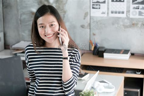 泰国美丽的年轻亚洲女商人讲智能电话带着快乐的情绪微笑在家工作办公室临时生活方式概念在办公室工作吸引人的高清图片下载-正版图片307608590-摄图网