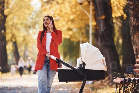 Talking by the phone. Mother in red coat have a walk with her kid in ...