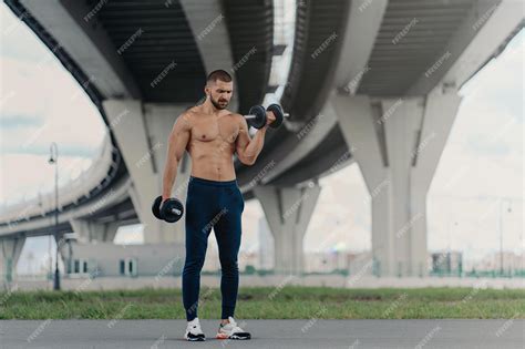 Premium Photo | Healthy strong bodybuilder lifts heavy barbells has workout outdoor demonstrates ...