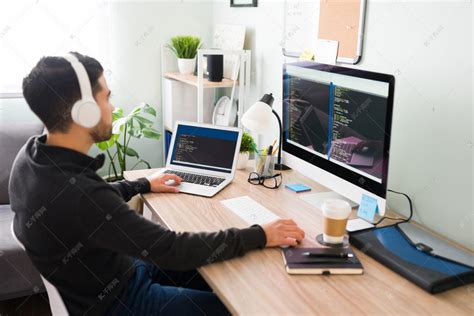 20多岁的年轻人在他的计算机上从事代码编写或程序员工作。坐在办公室桌上用耳机听音乐的拉丁人高清摄影大图-千库网