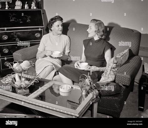 1950s TWO WOMEN SITTING ON SOFA HAVING CUP OF COFFEE VISITING TALKING ...