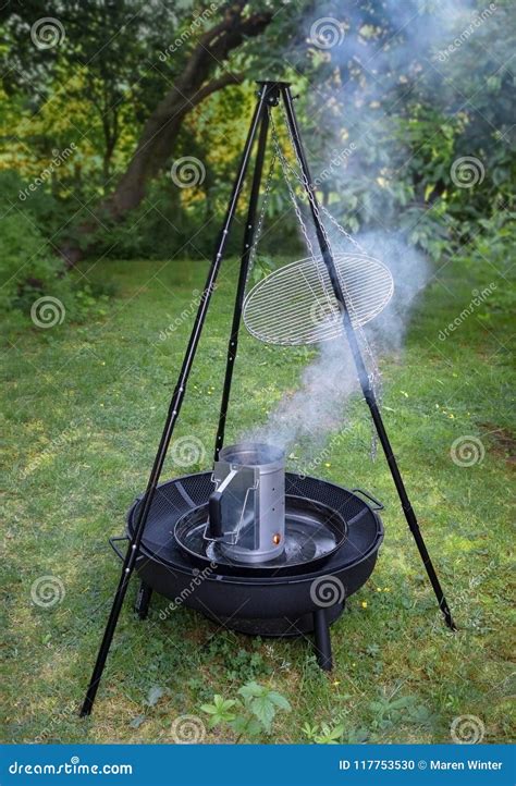Fuming Barbecue Charcoal Chimney Starter on a Black Tripod Swivel Grill ...